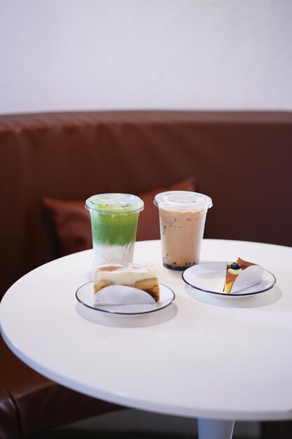 Zdjęcie szklanka lodowego matcha, zielonej herbaty latte i pęcherzyków herbaty mlecznej z niewyraźnym ciastem na białym stole w kawiarni