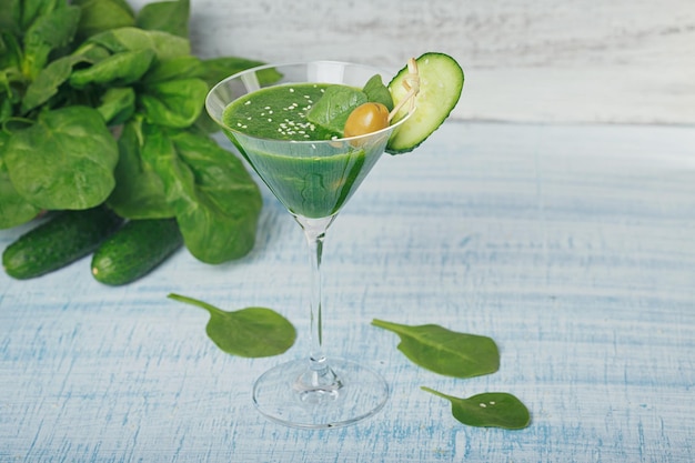 Szklanka Martini wypełniona świeżym zielonym koktajlem ze szpinaku i ogórka na jasnoniebieskim drewnianym tle. Napoje bezalkoholowe. Zdrowa żywność i koncepcja wegetariańska.