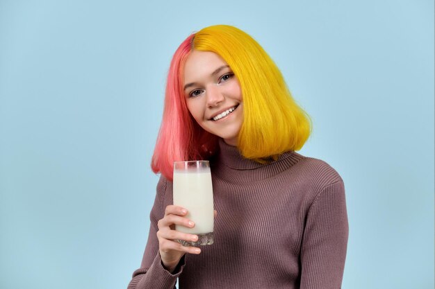 Zdjęcie szklanka mleka w ręku pięknej uśmiechniętej nastoletniej modelki na niebieskim tle studia