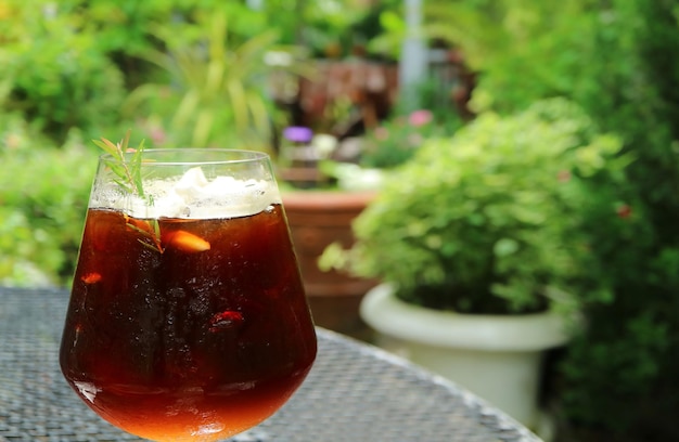 Szklanka mrożonej kawy z rozmytymi zielonymi liśćmi w tle