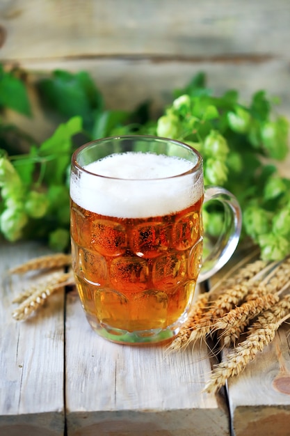Zdjęcie szklanka piwa pszenicznego na powierzchni drewnianych. kłosy pszenicy i chmiel.