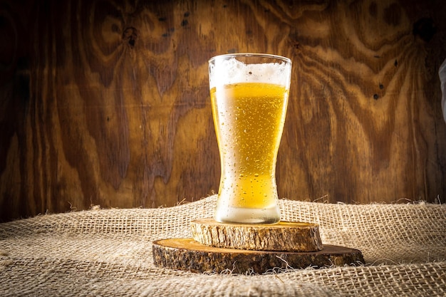 Szklanka piwa stoi na stosie drewna i kawałku drewna.