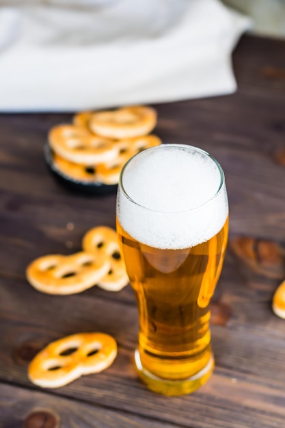 Szklanka piwa z pianką i słonymi precelkami na drewnianym stole Widok pionowy Zbliżenie