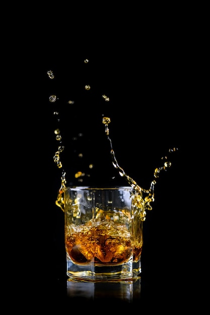 Szklanka rozpryskiwania whisky lub innego alkoholu z kostką lodu na czarnym tle