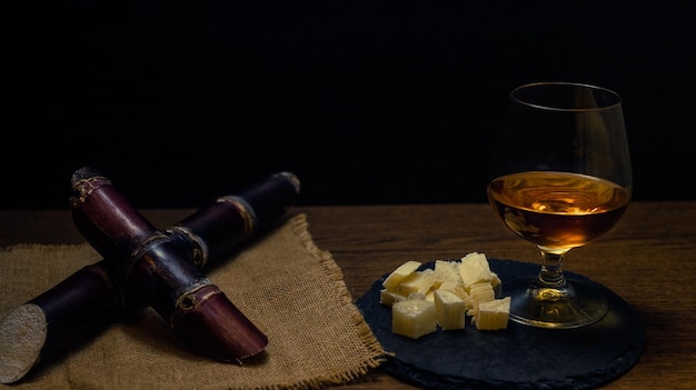 Zdjęcie szklanka rumu z trzciny cukrowej z kawałkami trzciny cukrowej na rustykalnym drewnianym stole i ciemnym tle