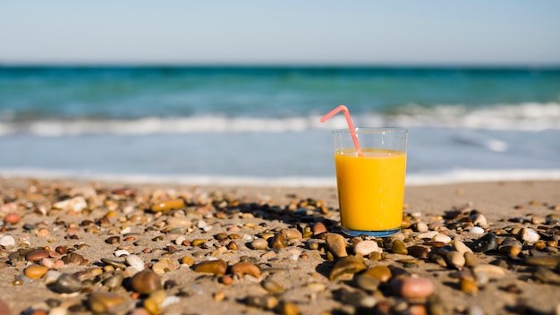 Szklanka soku mango ze słomką do picia na piasku na plaży