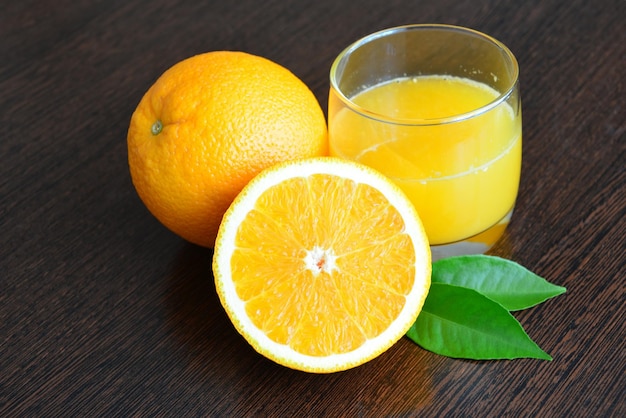 Szklanka soku pomarańczowego obok połówki pomarańczy z zielonymi liśćmi na białym tle