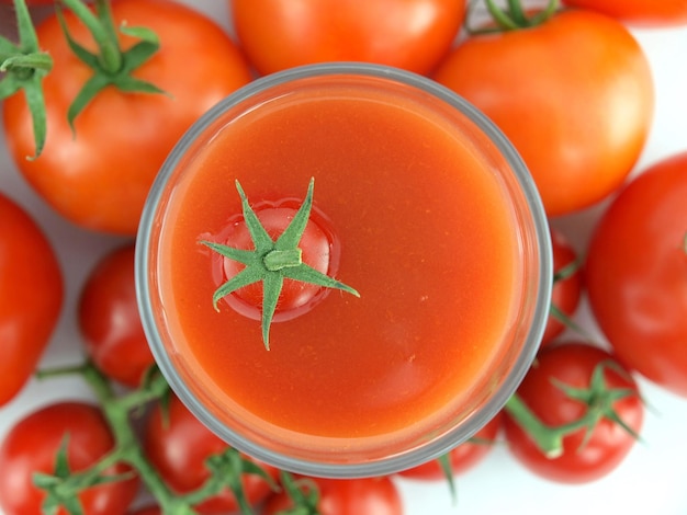 Szklanka soku pomidorowego z kilkoma pomidorami za nią.