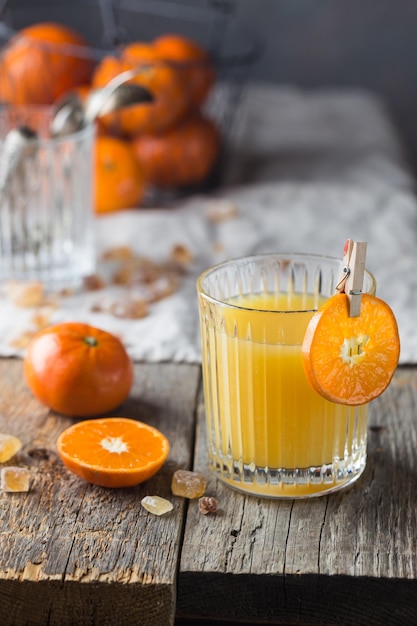 Szklanka świeżego soku mandarynkowego z dojrzałymi mandarynkami na starym drewnianym stole, w stylu rustykalnym