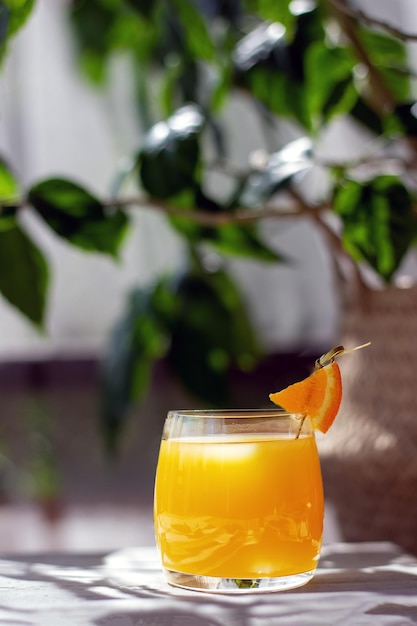 Szklanka świeżego soku pomarańczowego przyozdobiona plasterkiem pomarańczy na białym drewnianym stole na letnim tarasie