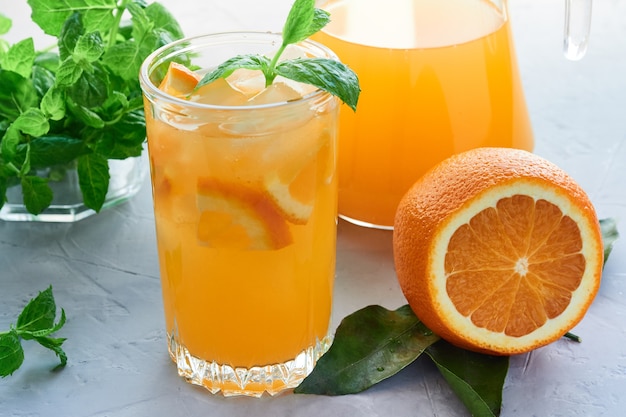 Szklanka świeżego soku pomarańczowego z owocami i liśćmi mięty na szarej powierzchni