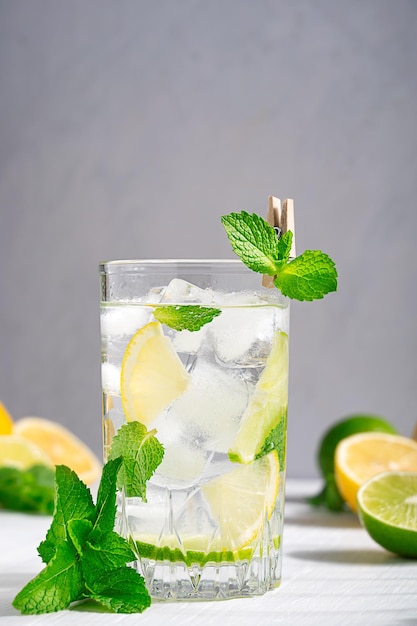 Szklanka świeżej zimnej kwaśnej lemoniady z plasterkami limonki i cytryny, listkiem mięty i lodem podawana na stole