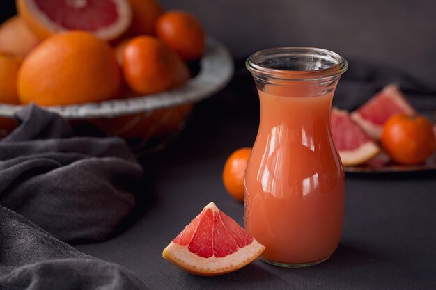 Szklanka świeżo wyciśniętego soku grejpfrutowego ze świeżymi owocami cytrusowymi na ciemnym tle. Grejpfruty, pomarańcze i mandarynki