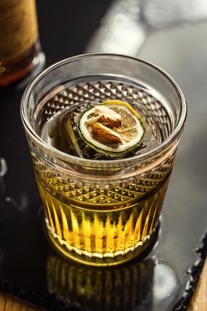 Szklanka whisky koniaku lub brandy z cytryną i kostkami lodu stojąca na blacie barowym z butelką w tle