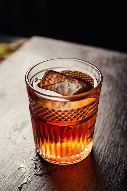 Szklanka whisky koniaku lub brandy z cytryną i kostkami lodu stojąca na blacie baru