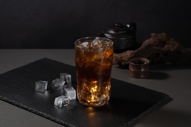 Szklanka whisky stoi na czarnej tacy z kostkami lodu.