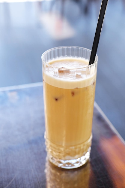Szklanka z latte i czarnymi słomkami stoi na stole z metalową powłoką na letnim tarasie kawiarni Zdjęcie pionowe