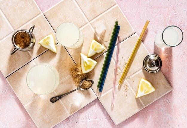 Szklanki z letnią lemoniadą i cukrem trzcinowym na różowym tle szklane słomki do napojów