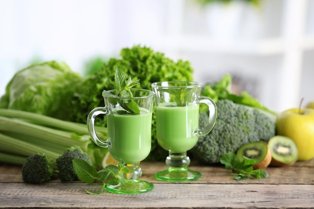 Szklanki zielonego zdrowego soku z warzywami i owocami na drewnianym stole