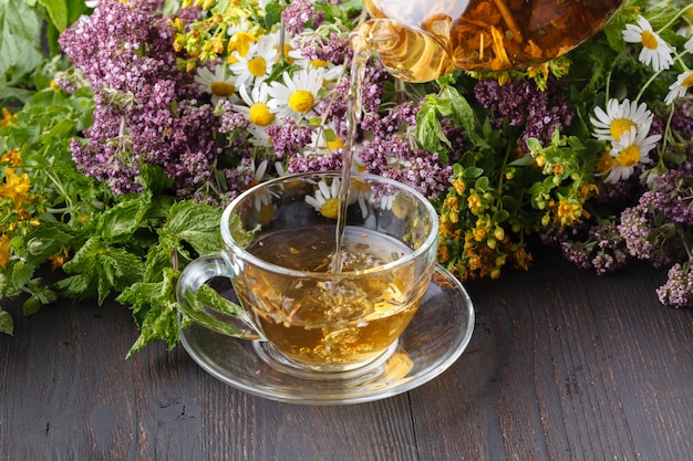 Szklany czajniczek i filiżanka z zieloną herbatą na starym drewnianym stole ze świeżymi ziołami