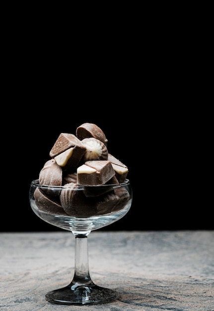 Szklany kubek wypełniony czekoladkami na czarnym tle