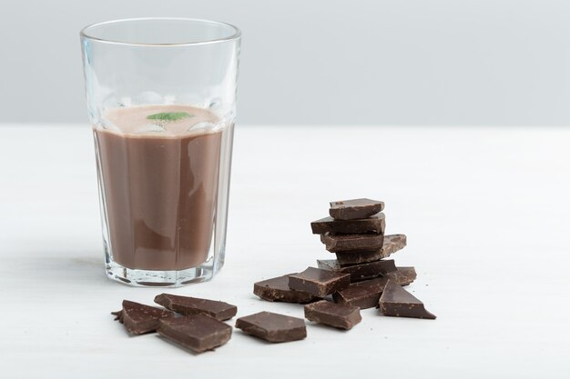 Szklany kubek z proteinowym shake'iem czekoladowym stoi na tle paczki białka na białym stole. Koncepcja żywienia sportowego.