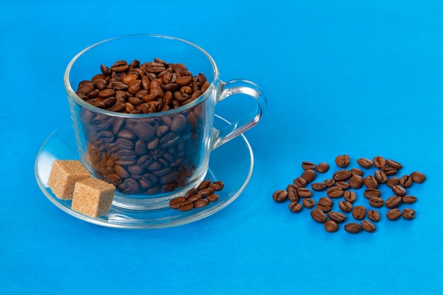 Szklany Przezroczysty Kubek Z Ziaren Kawy Z Kawałkami Surowego Cukru Posypany Ziarnami Kawy Na Niebiesko