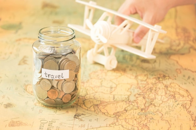 Zdjęcie szklany słoik z monetami i napisem podróży na mapie świata z drewnianym samolotem zabawkowym na stole koncepcja podróży i oszczędzanie pieniędzy