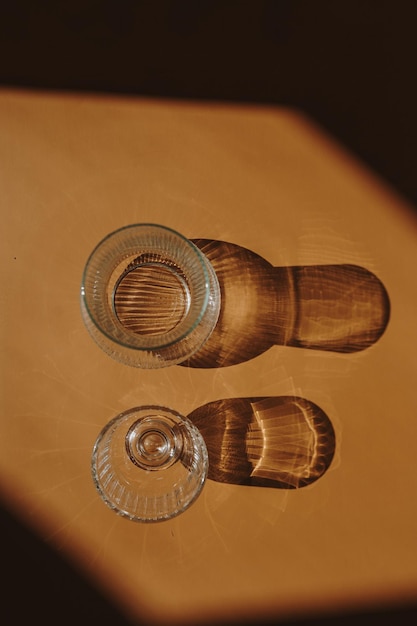 Szklany szampan i szklany wazon na ciepłym jasnobrązowym pomarańczowym tle z sylwetką w jasnych odcieniach słońca Estetyczna minimalistyczna kompozycja
