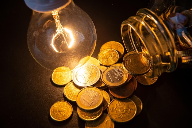 Zdjęcie szklany wazon z monetami i żarówką obok oszczędzając na rachunkach za usługi elektryczne
