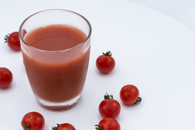 Zdjęcie szkło świeży organicznie pomidorowy sok z surowymi pomidorami na bielu talerzu.