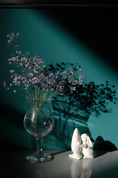 Szkło z fioletowymi kwiatami i solniczka w kształcie królika ze słońcem i cieniem na zielonej ścianie
