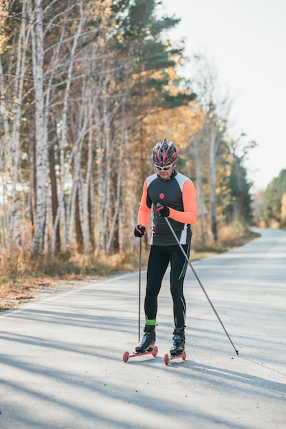 Szkolenie sportowca na wrotkach Biathlon jazda na nartorolkach z kijkami w kasku Jesienny trening Sport na rolkach Dorosły mężczyzna jeżdżący na łyżwach