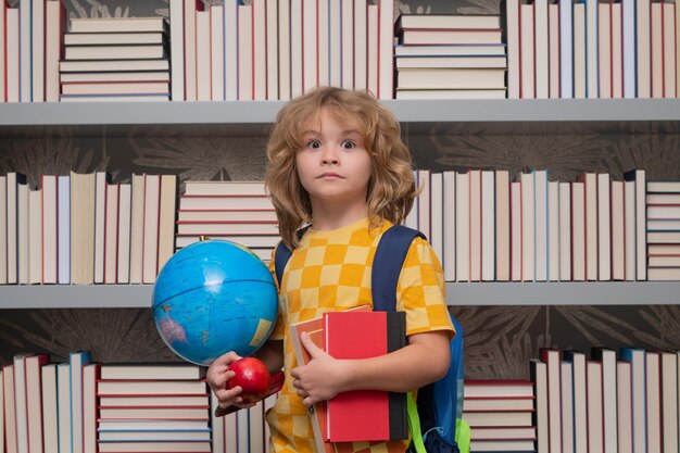 Szkolna chłopiec z światową kulą ziemską i książkami dziecko w wieku szkolnym studiujące w klasie w szkole podstawowej ul