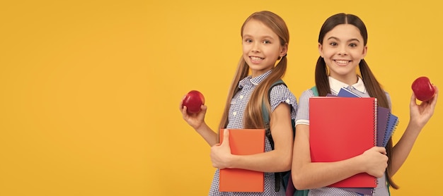 Szkolne dziewczyny przyjaciele Szczęśliwi uczniowie z książkami trzymają witaminy organiczne jabłka żółte tło w szkole