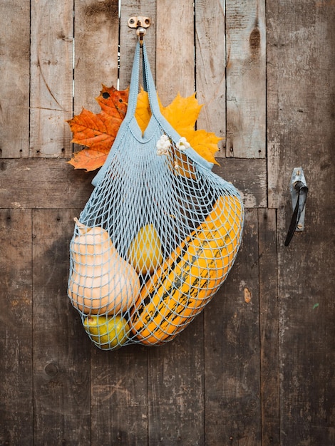 Sznurkowa torba na zakupy z jesiennymi zbiorami wisząca na starych rustykalnych drewnianych drzwiach