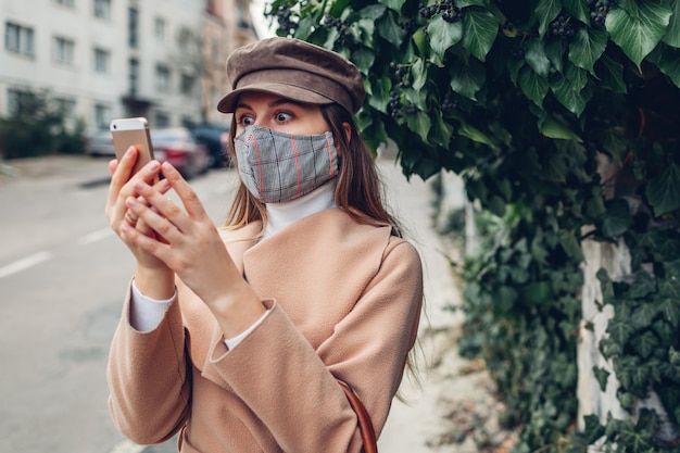 Szokujące wiadomości. Kobieta nosi maskę na zewnątrz podczas pandemii koronawirusa covid-19 za pomocą telefonu
