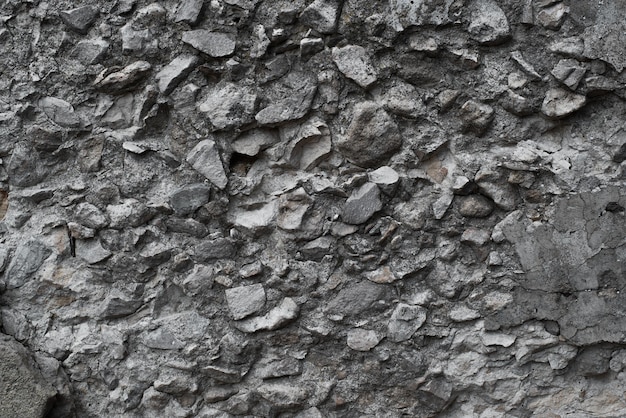 Szorstka ciemnoszara kamienna ściana wykonana z kostki brukowej i betonu Tekstura nierówne kamienne tło