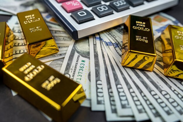 Sztabki złota leżą z kalkulatorem w pobliżu dużej sumy izolowanych dolarów