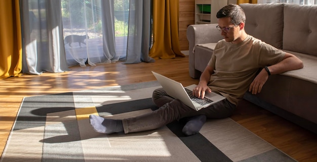 Sztandar przedstawiający młodego mężczyznę siedzącego przy komputerze i pracującego na podłodze w słonecznym mieszkaniu na poddaszu Praca z domu Nauka online