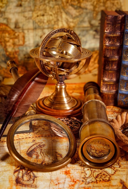 Sztuka martwa. Kłamstwa ze szkła powiększającego w stylu vintage, zegarek kieszonkowy, stara książka i astrolabium na starożytnej mapie świata w 1565 roku.