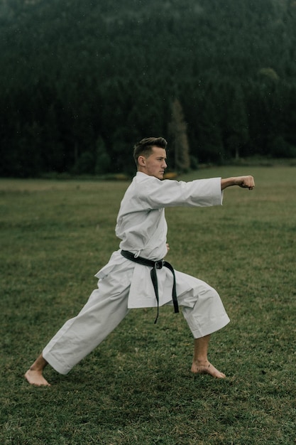 Sztuka walki karate mężczyzna w kimonie z trenami z czarnym pasem na wolnej od gór przestrzeni