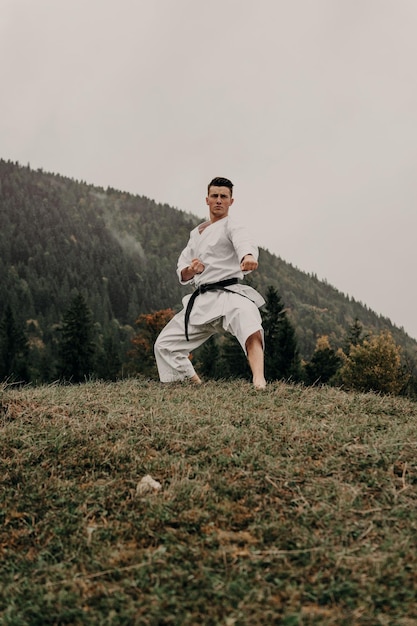 Sztuka walki karate mężczyzna w kimonie z trenami z czarnym pasem na wolnej od gór przestrzeni