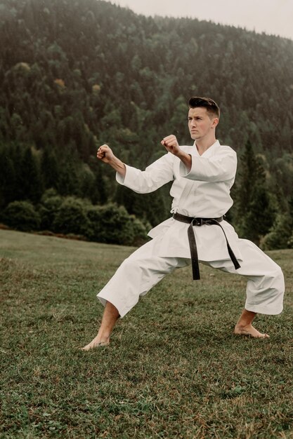 Sztuka walki karate mężczyzna w kimonie z trenami z czarnym pasem na wolnej od gór przestrzeni