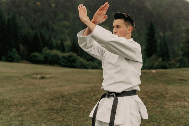 Sztuka walki karate mężczyzna w kimonie z trenami z czarnym pasem na wolnej od gór przestrzeni