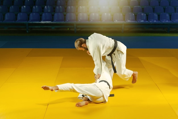 Sztuki walki. Oszczędzanie Porterów. Sportowy mężczyzna i kobieta w białym kimonie trenują rzuty judo i chwytają w hali sportowej