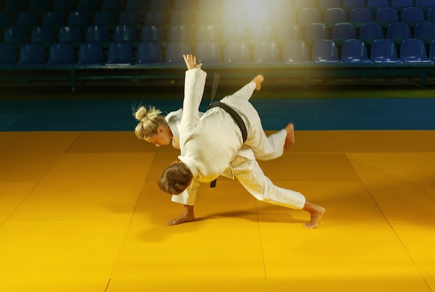 Sztuki walki. Oszczędzanie Porterów. Sportowy mężczyzna i kobieta w białym kimonie trenują rzuty judo i chwytają w hali sportowej