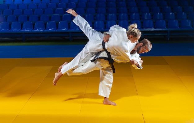 Sztuki walki. Oszczędzanie portierów. Sport mężczyzna i kobieta w białym kimono pociąg judo rzuca i chwyta w hali sportowej