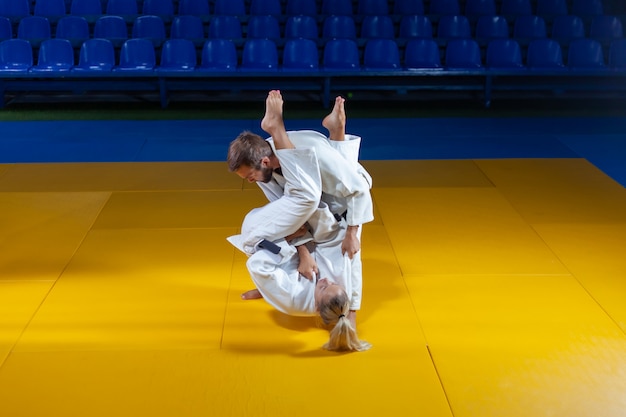 Sztuki walki. Oszczędzanie portierów. Sport mężczyzna i kobieta w białym kimono pociąg judo rzuca i chwyta w hali sportowej