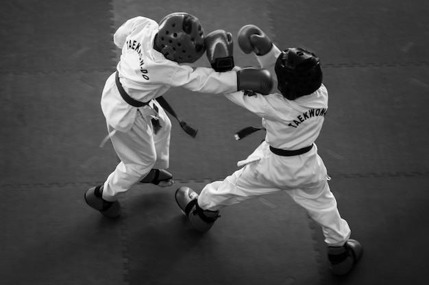 Sztuki walki Taekwondo Dzieci w tradycyjnych kaskach kimano i rękawiczkach Pojedynek sportowy Czarno-biały Dla nastrojowego efektu szumu filmu Tekst Taekwondo to nazwa sztuki walki